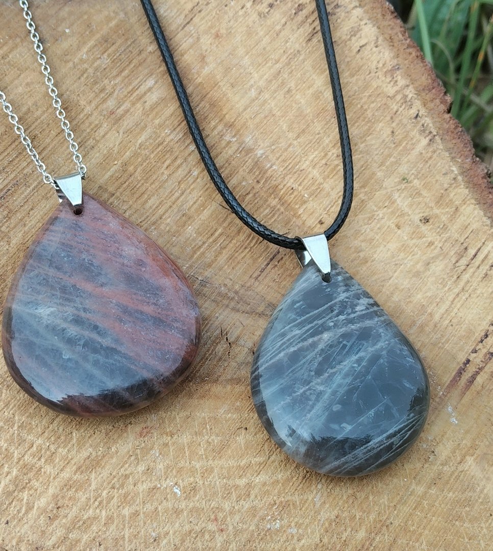deux-pendentifs-en-forme-de-goutte-en-pierre-naturelle-polie-l-un-sur-chaine-argentee-l-autre-sur-cordon-noir-poses-sur-une-tranche-de-bois-invite-au-calme-a-l-ancrage-et-a-l-equilibre-emotionnel.jpeg Pendentif pierre de lune noire – Image 1