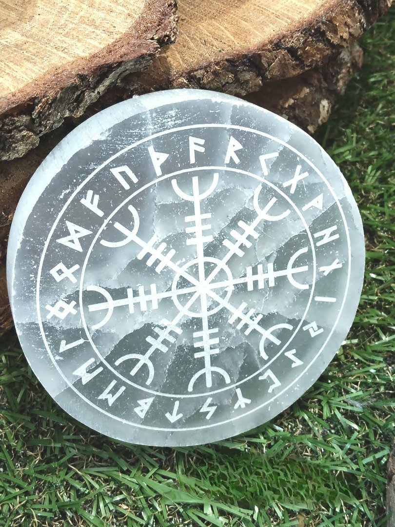 plateau-rond-en-selenite-grave-vegvisir-et-runes-pose-sur-herbe-avec-rondin-de-bois-en-decor-favorise-purification-protection-et-recentrage.jpeg Plateau sélénite boussole vegvisir – Image 1